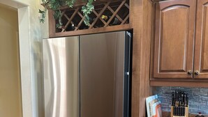 Un refrigerador de acero inoxidable con un espacio para vinos encima, armarios de madera, una encimera de granito y un bloque para cuchillos.