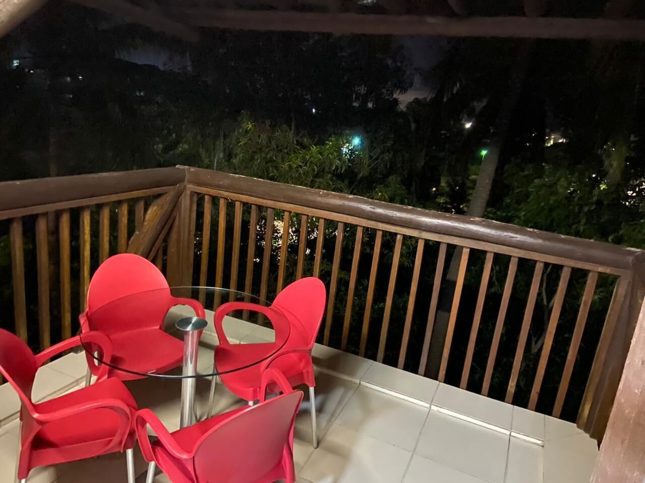A balcony with a wooden railing, a glass table, and four red chairs.
