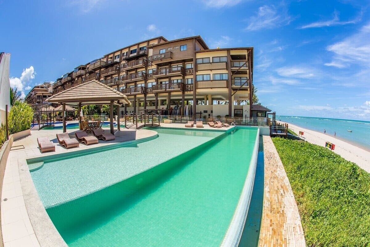 A hotel with a swimming pool, lounge chairs, and a beach view.