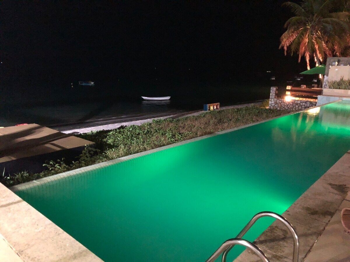 A nighttime swimming pool with a green hue, a small boat in the background, and a palm tree.