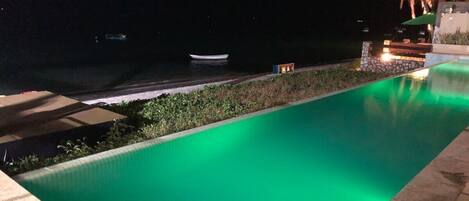 A nighttime swimming pool with a green hue, a small boat in the background, and a palm tree.
