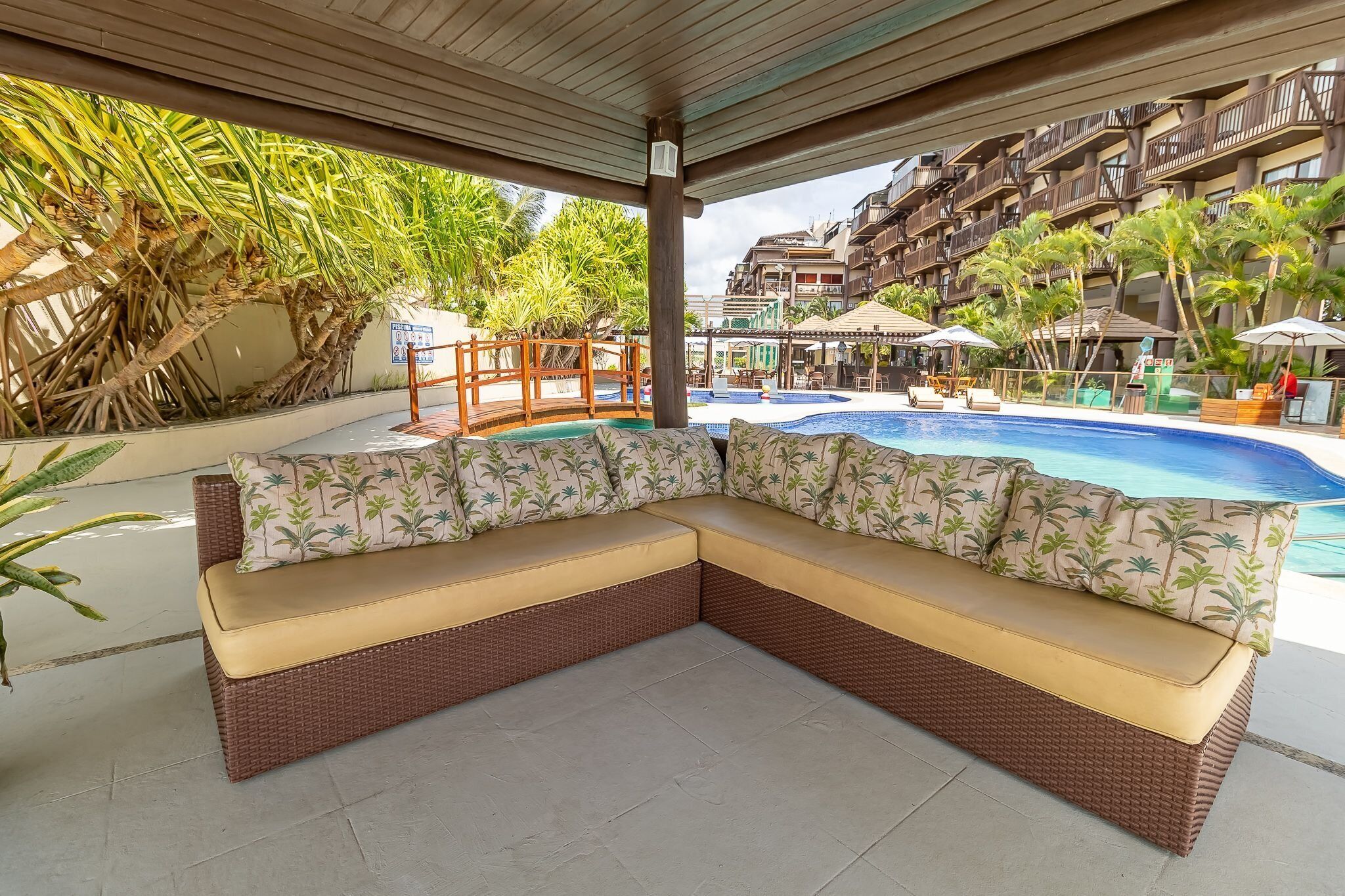 A covered outdoor seating area with a pool in the background.