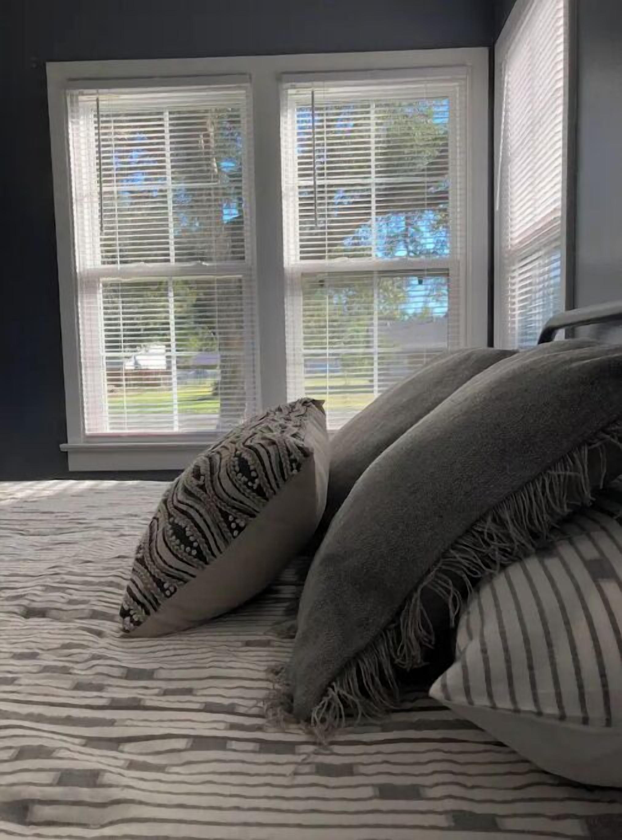 A bedroom with a bed, two pillows, and a window with blinds.