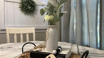 Une table à manger ornée d’un vase blanc contenant des fleurs, d’un livre intitulé « SIMPLY, DANTLY » et d’un plateau en bois sur lequel repose une lettre en bois, la lettre « A ».