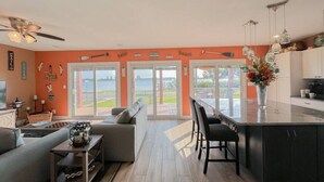 Una sala moderna con un sofá, una mesa de centro y un comedor con sillas. Hay un ventanal con vistas al exterior.