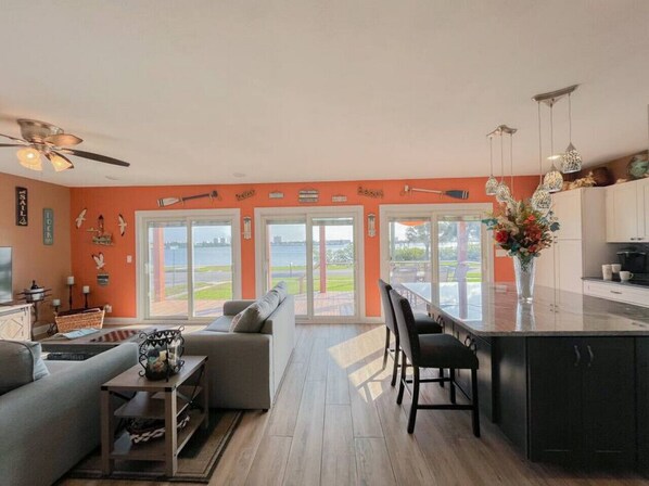 Ein modernes Wohnzimmer mit einer Couch, einem Couchtisch und einem Essbereich mit Stühlen. Ein großes Fenster bietet einen Ausblick ins Freie.