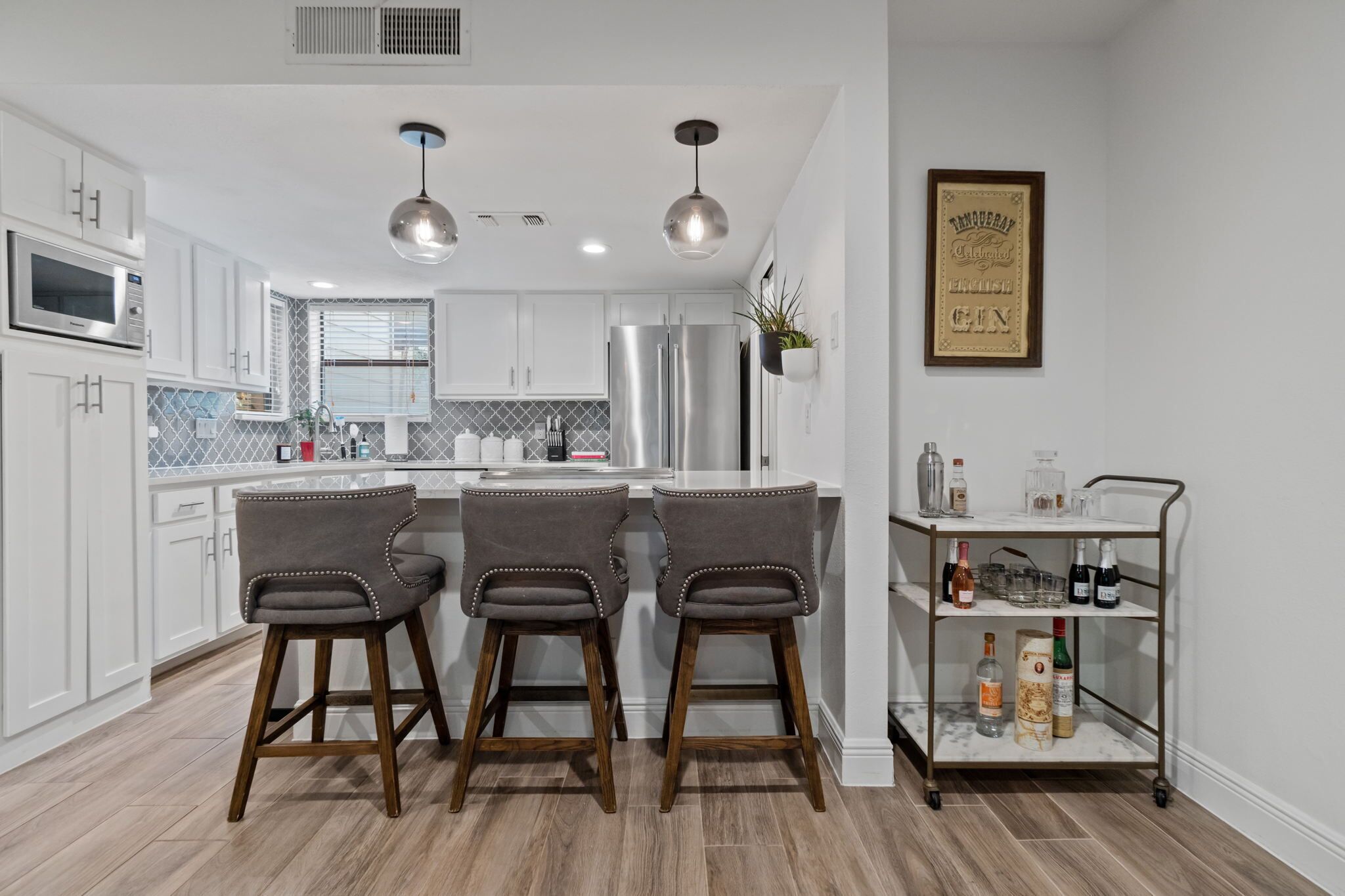A modern kitchen with white cabinets, stainless steel appliances, and a bar area with stools.