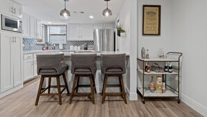 Une cuisine moderne avec des meubles blancs, des appareils en acier inoxydable et un coin bar équipé de tabourets.