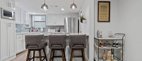 A modern kitchen with white cabinets, stainless steel appliances, and a bar area with stools.