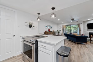 A modern kitchen with an island, a dining area with a sofa, and a fireplace. - Cool Off in Barton Springs Pool Steps from Zilker Park (Austin)