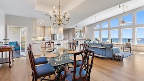 A spacious living area with a large dining table, comfortable seating, and a view of the ocean.