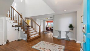 A spacious living area with a wooden staircase, a decorative fish sculpture, and a blue door. - Carpe Beachiem Home, Ocean Views & Dual Decks (Ponte Vedra Beach)