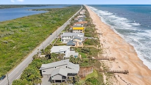 A coastal residential area with houses along a beachfront, a road parallel to the beach, and a wooden boardwalk leading to the shore.
