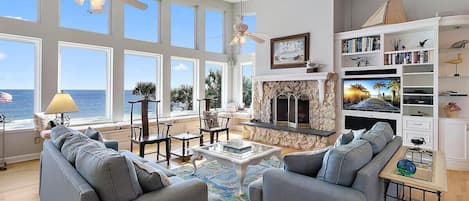 A spacious living room with a fireplace, large windows, and a view of the ocean.