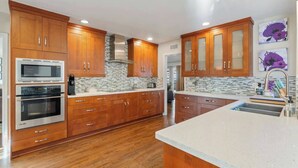 A modern kitchen with wooden cabinets, two ovens, a stainless steel range hood, and a granite countertop. - 🌴Spacious & Private 5Bdr Private Retreat-Saltwater Pool/Spa, Outdoor Kitchen🌴 (Los Angeles)