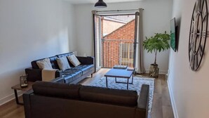 A modern living room with a black sofa, a coffee table, and a large window with a view of a brick building. - Best Location in Belfast! Free Parking-Luxury Accommodation (Belfast)