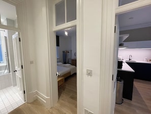 A hotel room with a bed, a small bedside table, a window, and a view of the adjacent kitchen area. - Chic 1BD City Stay in the Heart of London (London)