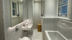 Un baño moderno con azulejos blancos, lavamanos, inodoro y bañera.