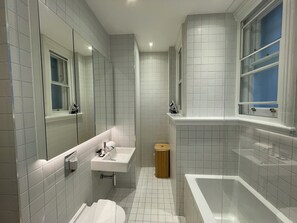 Une salle de bain moderne avec des carreaux blancs, un lavabo, des toilettes et une baignoire.