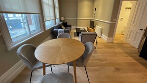 Una sala de estar moderna con una mesa redonda de madera, sillas tapizadas en gris, un sofá y un televisor.