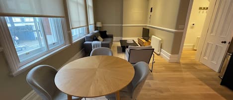 Un salon moderne avec une table ronde en bois, des fauteuils à revêtement gris, un canapé et un téléviseur.
