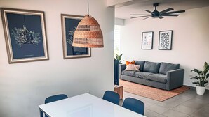 En moderne stue med en grå sofa, et hvidt spisebord med blå stole, og en hængende lysarmatur i flet.