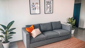 En grå sofa med to puder, et indrammet kunstværk over sofaen, og en potteplante til venstre.