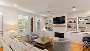 A living room with a sofa, armchairs, a coffee table, a fireplace, and a TV mounted on the wall. - Beach Chickens is your vacation destination for Pool Side Relaxation (St. Simons Island)