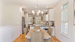 A spacious kitchen with a dining area, featuring a central island, white cabinetry, and a chandelier. - Beach Chickens is your vacation destination for Pool Side Relaxation (St. Simons Island)