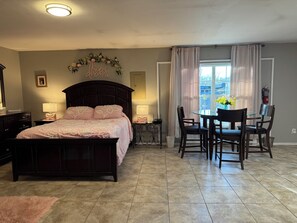 Un dormitorio con cama, mesitas de noche, escritorio, sillas y ventana con cortinas.