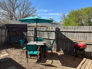 Un patio trasero con una terraza de madera, una parrilla y un porche cubierto con sillas y un paraguas.