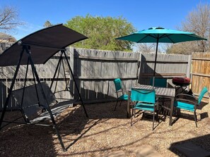 Un patio con mesa y sillas, un columpio y una parrilla.