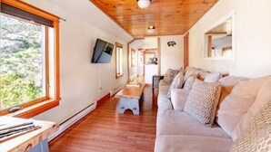 Ein modernes Wohnzimmer mit Holzboden, einem beigen Sofa, einem Couchtisch und einem an der Wand befestigten Fernseher.