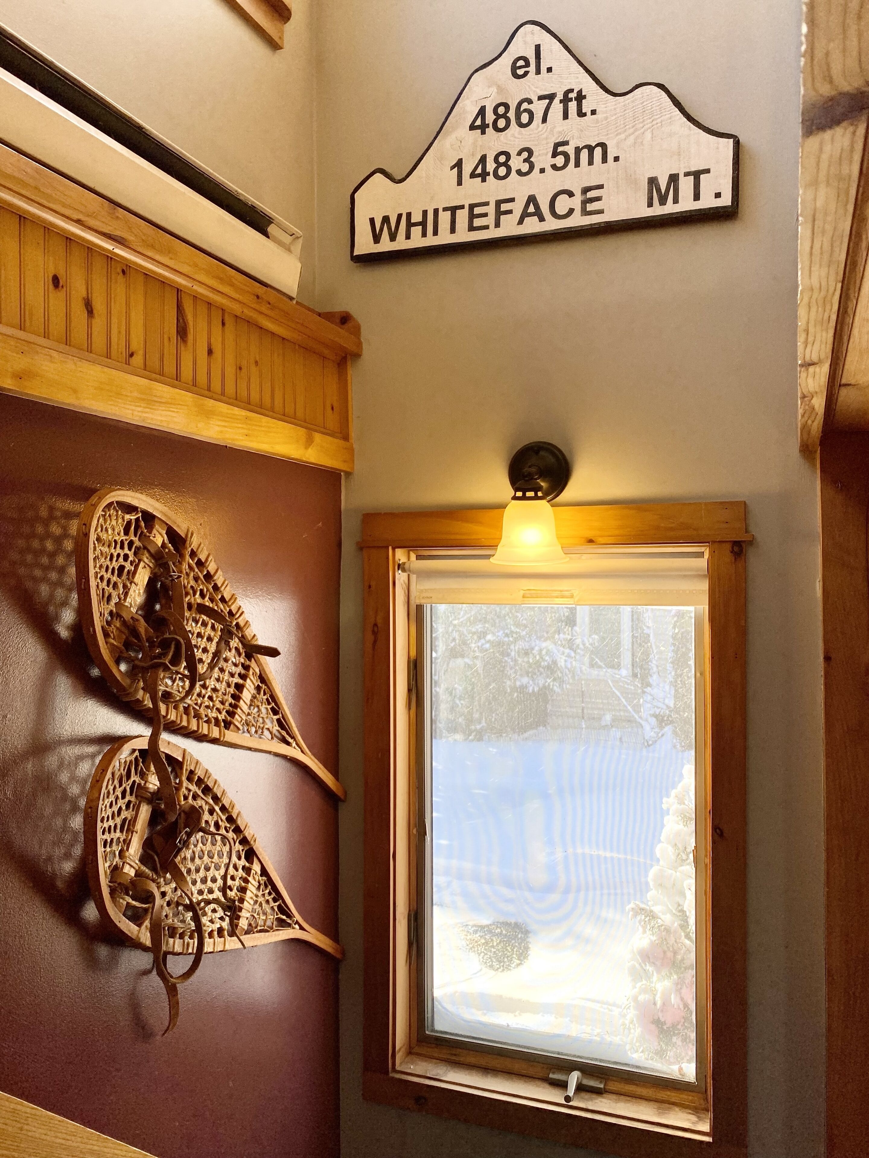 A wooden wall with a sign indicating Whiteface Mountain elevation and a window with a view of a snowy landscape.