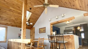 Ein Holzinterieur mit Essbereich, Deckenventilator und durch einen offenen Durchgang sichtbarer Küche.
