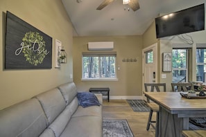 A living room with a gray sofa, a wooden dining table, and a TV mounted on the wall. - Secluded Butte Meadows Cabin w/ Deck & Grill! (Butte Meadows)