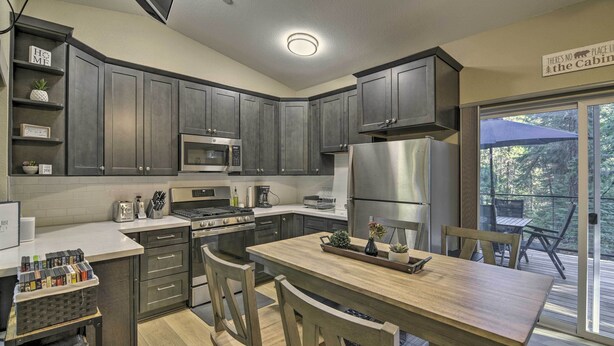 A modern kitchen with dark cabinets, stainless steel appliances, and a wooden dining table. - Secluded Butte Meadows Cabin w/ Deck & Grill! (Butte Meadows)
