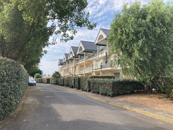 A row of modern, multi-story hotel buildings with balconies, surrounded by well-maintained hedges and trees.