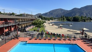 Un hotel con piscina, playa y montañas al fondo.