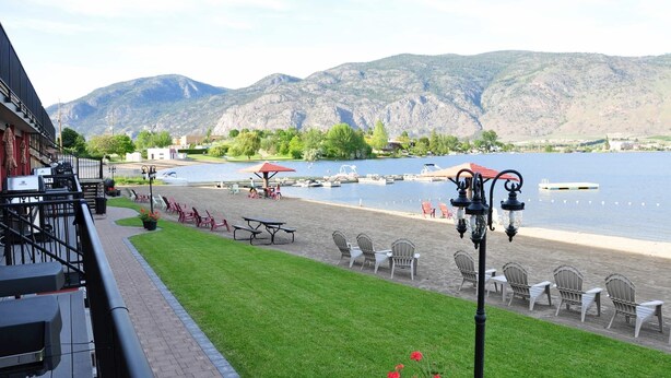 Un patio junto al lago con mobiliario exterior, una mesa de picnic y vistas a las montañas al fondo.