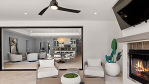A modern living room with a fireplace, a dining area, and a kitchen visible through an open door. - Multi-Million $ Resort-Style Estate w/Pickleball (Scottsdale)
