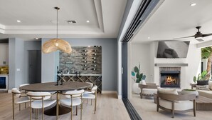 A modern living room with a round dining table, comfortable seating, a fireplace, and a wine rack. - Multi-Million $ Resort-Style Estate w/Pickleball (Scottsdale)