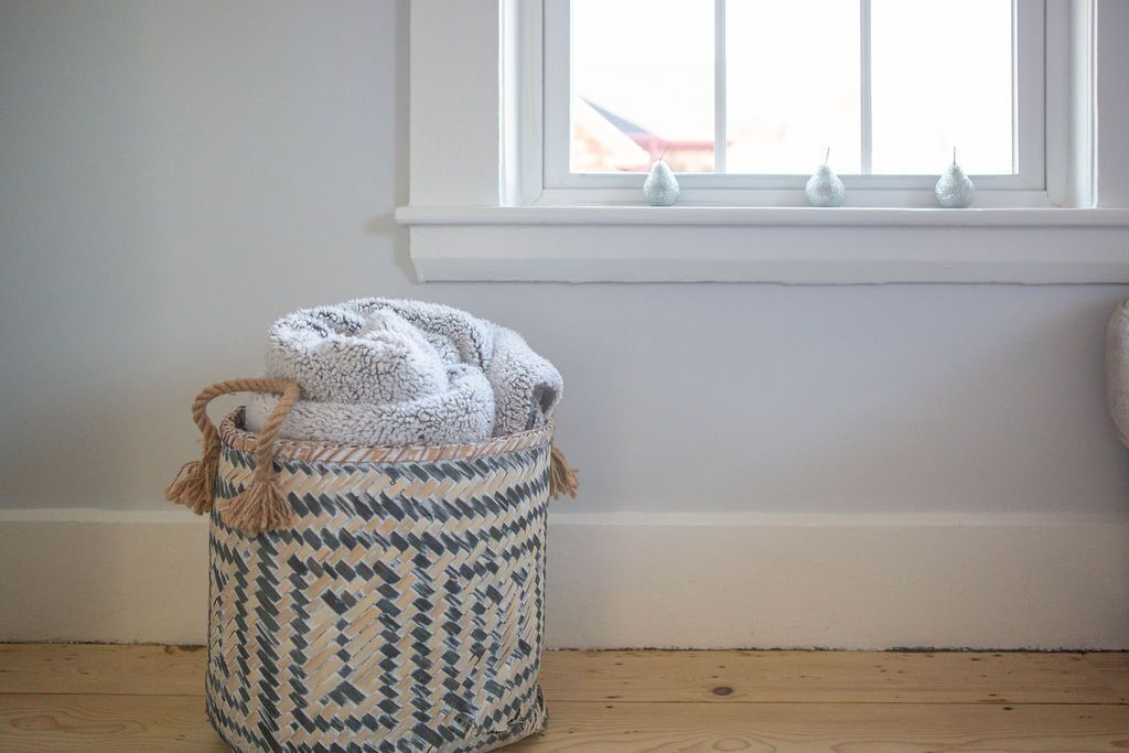 Une pièce avec un rebord de fenêtre orné d’objets décoratifs, un panier en osier doté d’une anse et un plancher en bois.