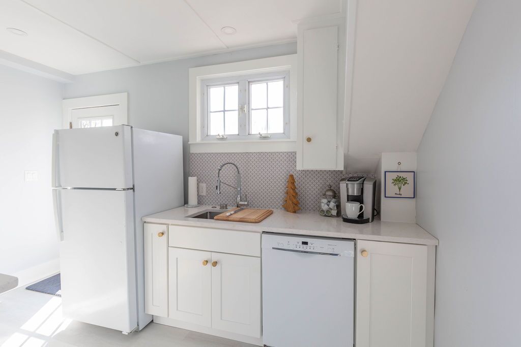 Une cuisine moderne avec des meubles blancs, un lave-vaisselle encastré, une fenêtre au-dessus de l’évier et une machine à café posée sur le plan de travail.