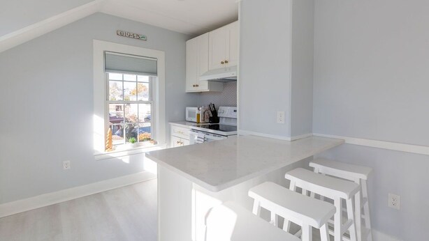 Une cuisine moderne avec des meubles blancs, un îlot central doté de tabourets de bar et une fenêtre donnant sur l’extérieur.