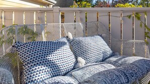 Un espace extérieur aménagé avec des sièges blancs, délimité par une clôture blanche et agrémenté d’un tissu à motifs bleus et blancs.