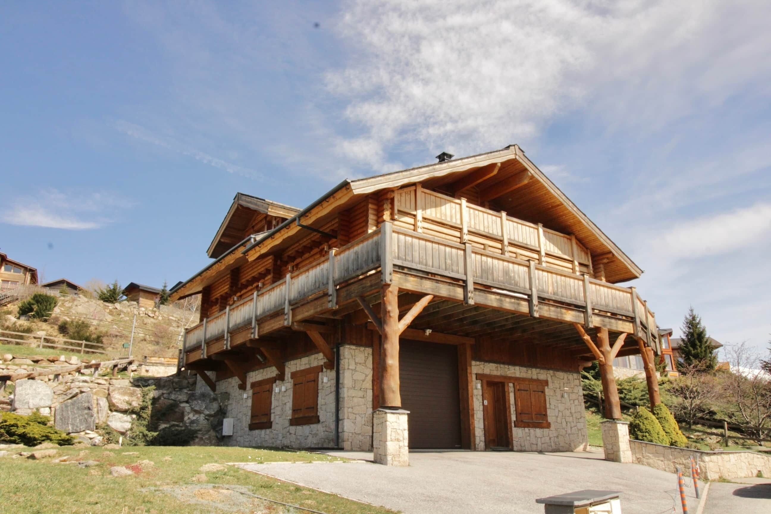 A two-story wooden building with a balcony, stone foundation, and a garage.