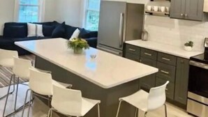 Une cuisine moderne dotée d’un îlot central, de tabourets de bar, de luminaires suspendus et d’un réfrigérateur encastré.