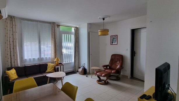 Una sala de estar con un sofá, sillas amarillas, una mesa, un sillón de cuero marrón, una lámpara y un televisor.