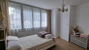 Un dormitorio con cama, mesita de noche, cómoda y ventana con cortinas.